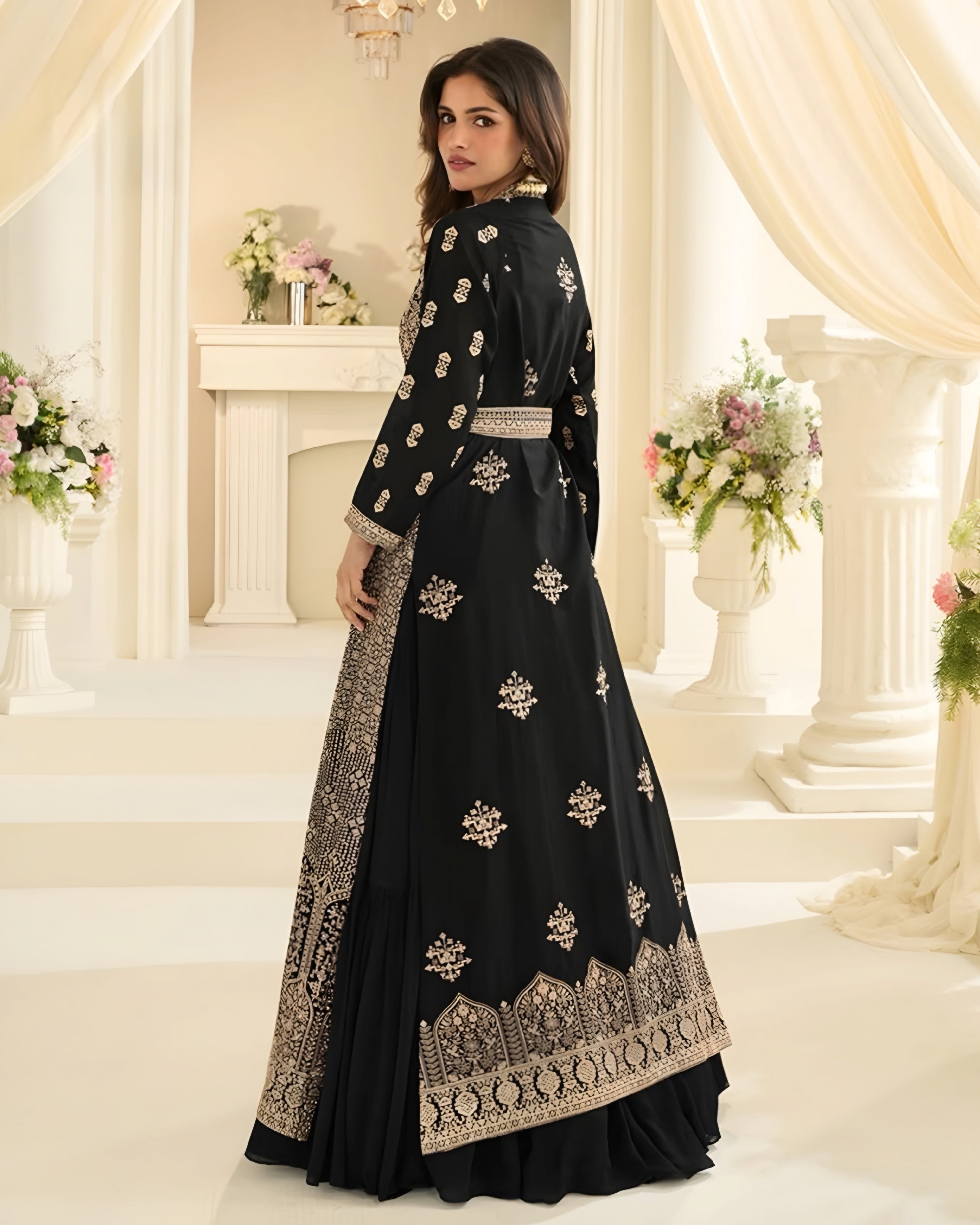 Woman wearing a black embroidered dress in a decorated room with flowers and columns.