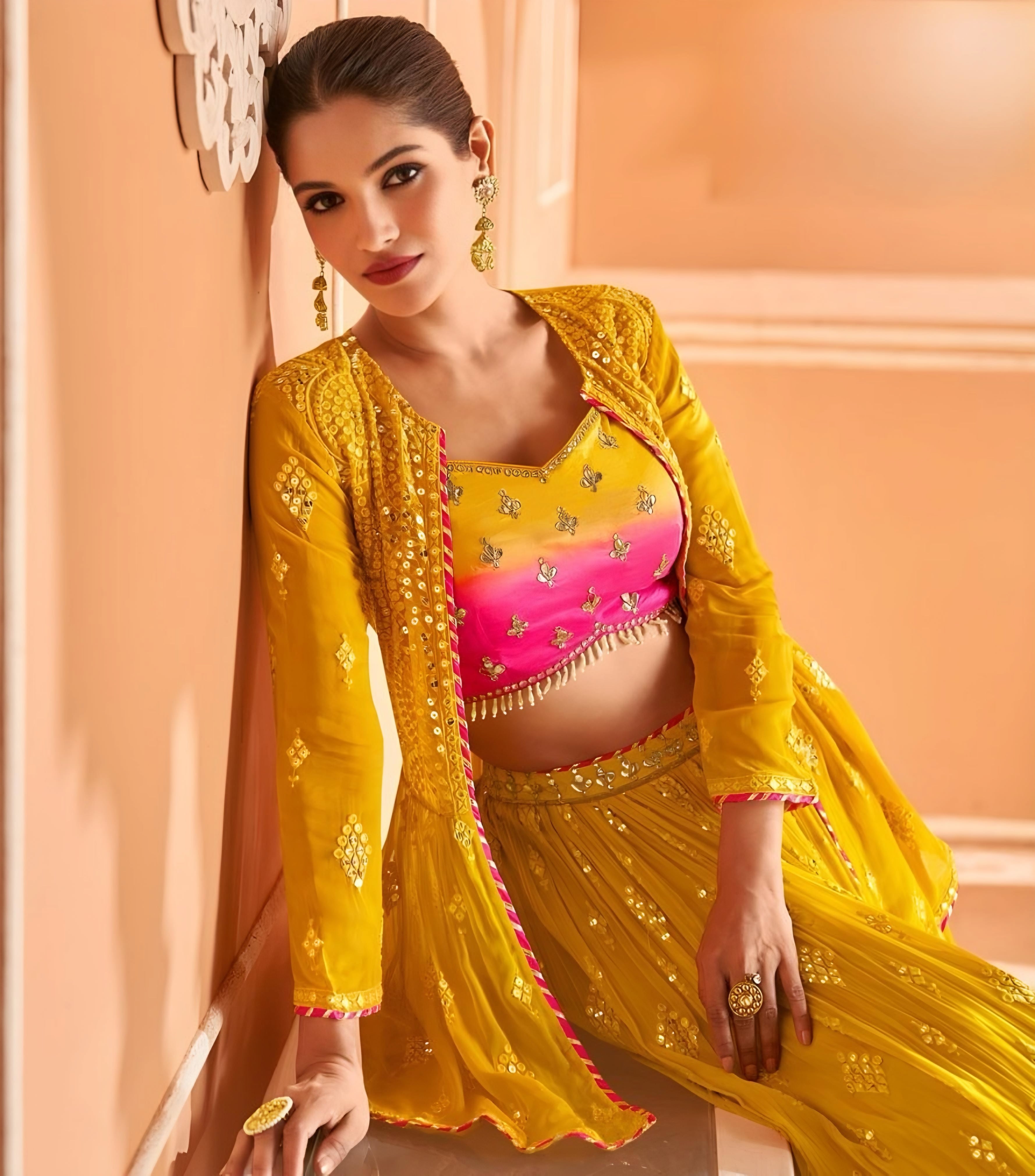 Woman seated in mustard yellow lehenga choli with long-sleeved jacket