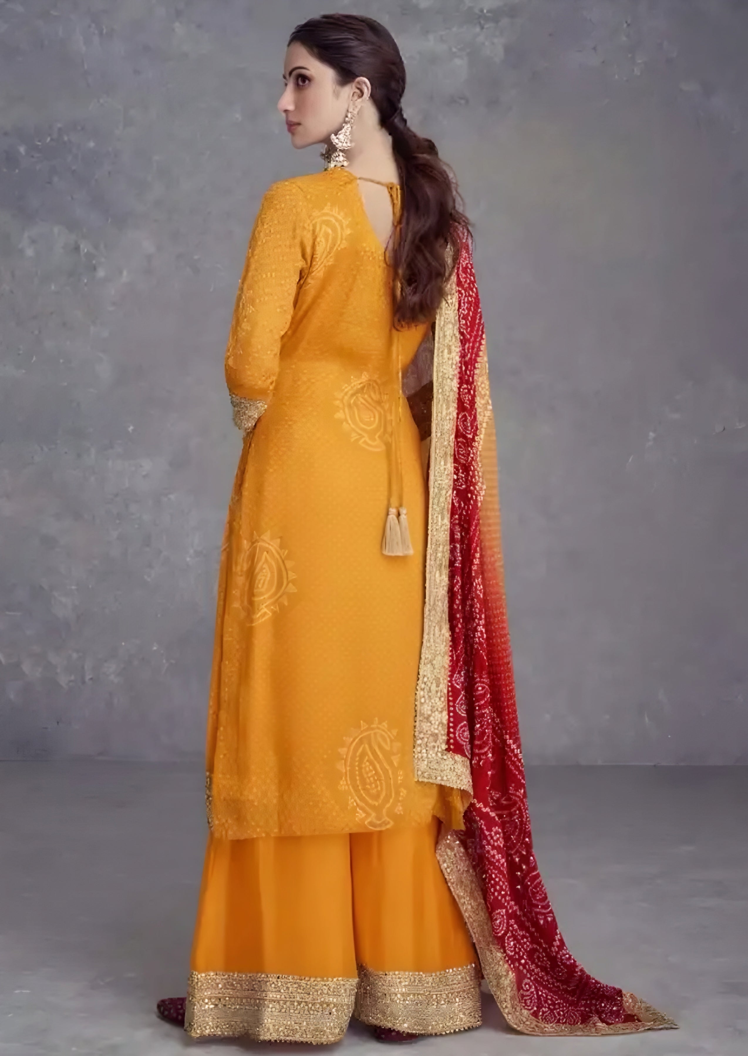 Woman wearing a mustard yellow outfit with a red dupatta against a gray background