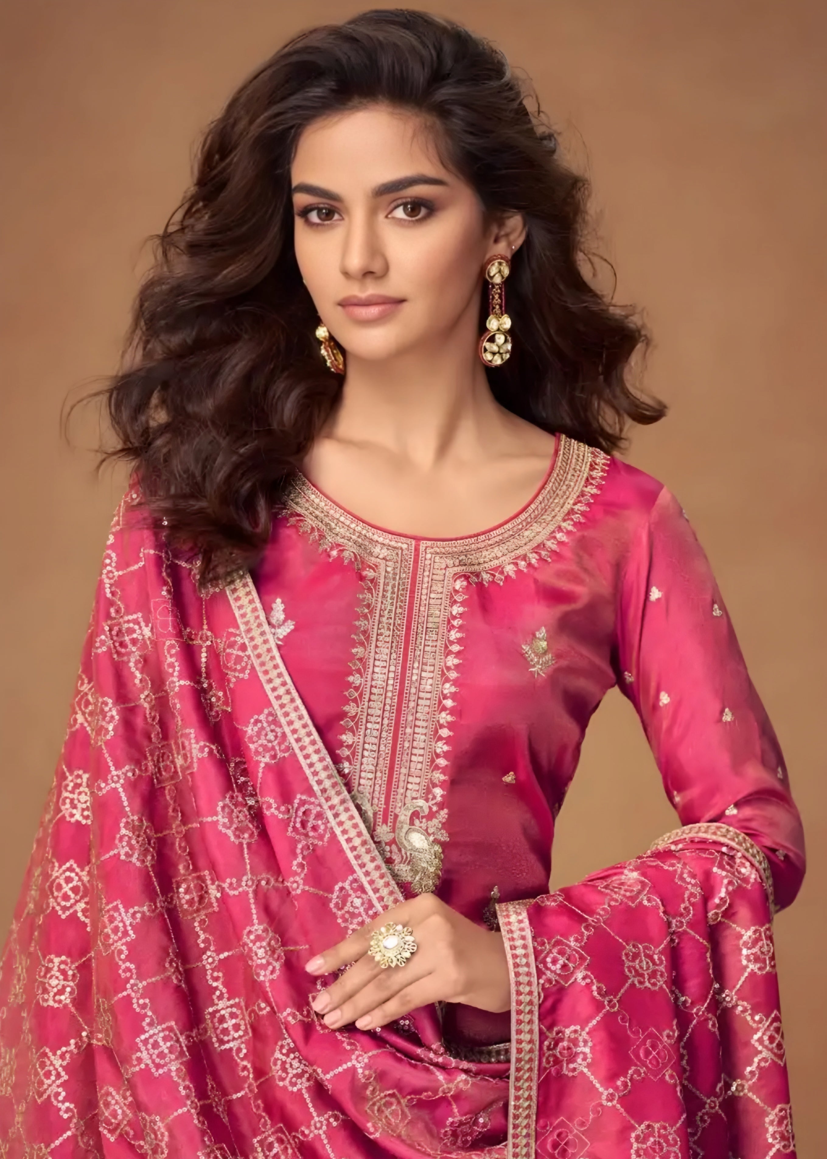Woman wearing a pink traditional outfit with intricate designs on a brown background