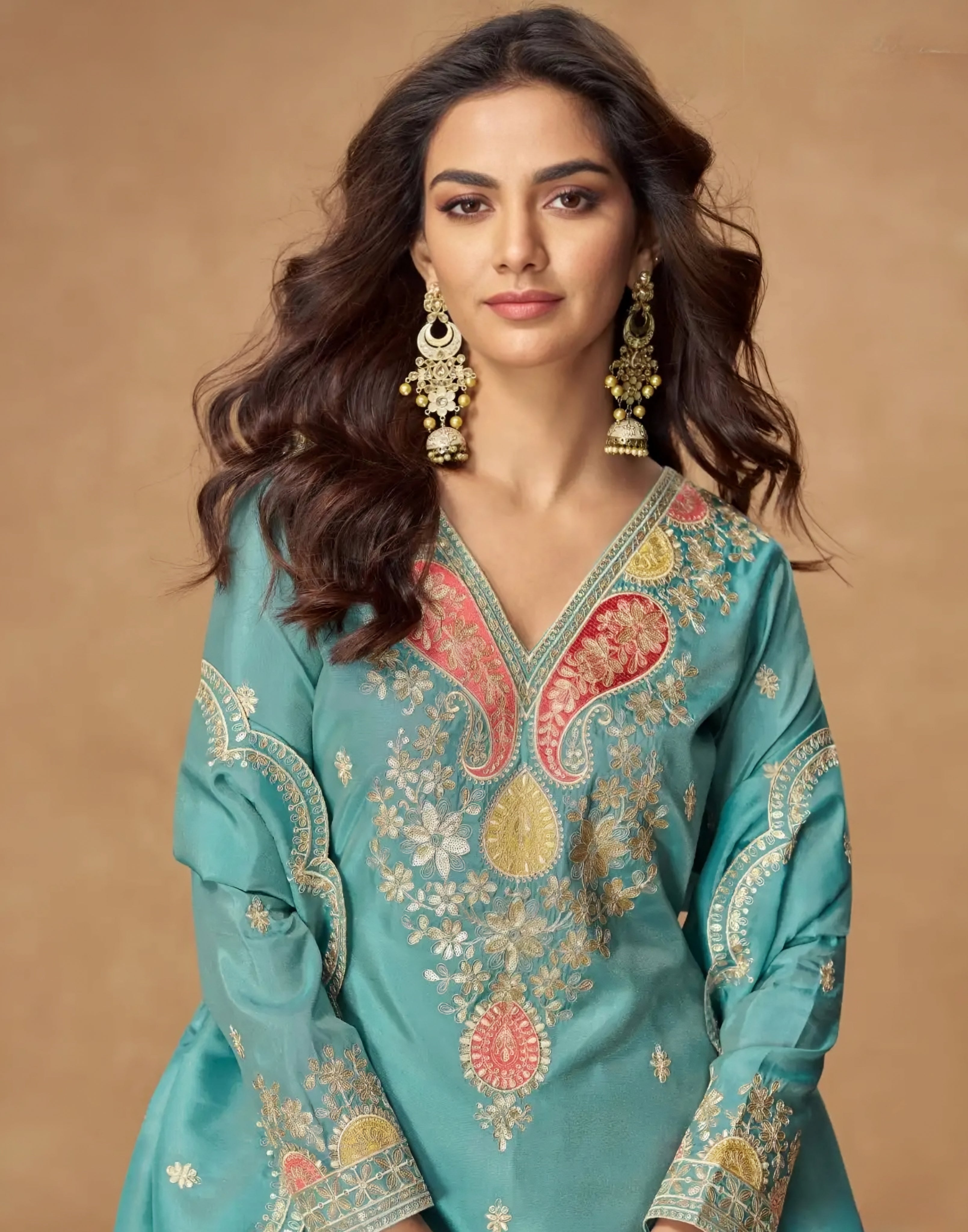 Woman wearing a teal embroidered traditional outfit with gold jewelry against a beige background