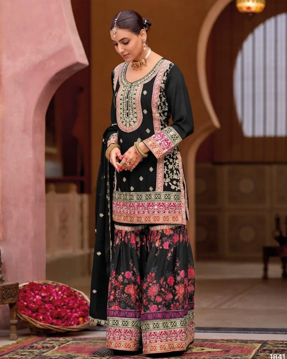 Woman in a traditional black and floral dress with intricate patterns in an ornate setting.
