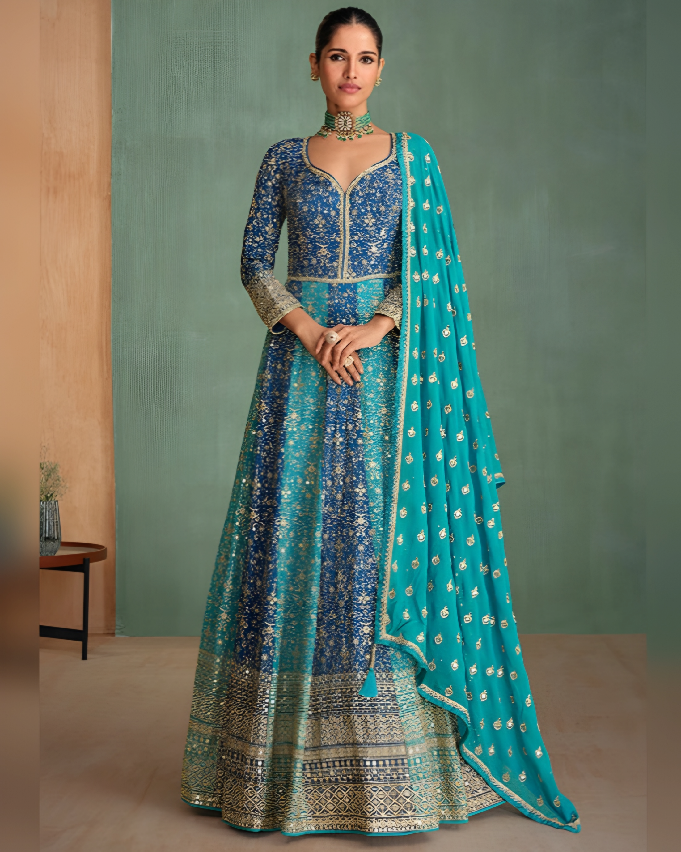 Woman wearing a blue and green traditional outfit with a matching dupatta against a plain background