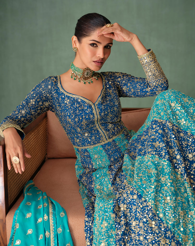 Woman in a traditional blue and green embroidered outfit sitting on a couch.