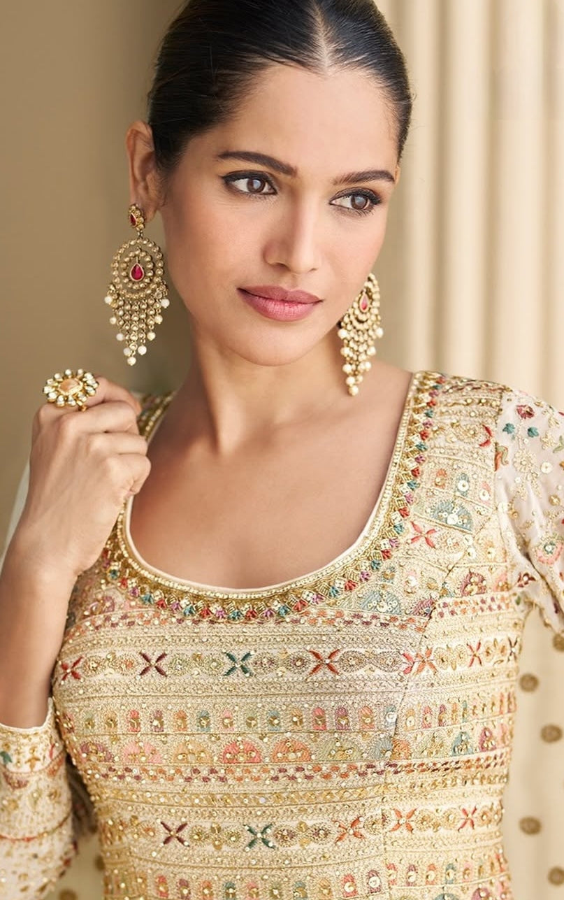 Woman wearing traditional embroidered attire with jewelry against a neutral background