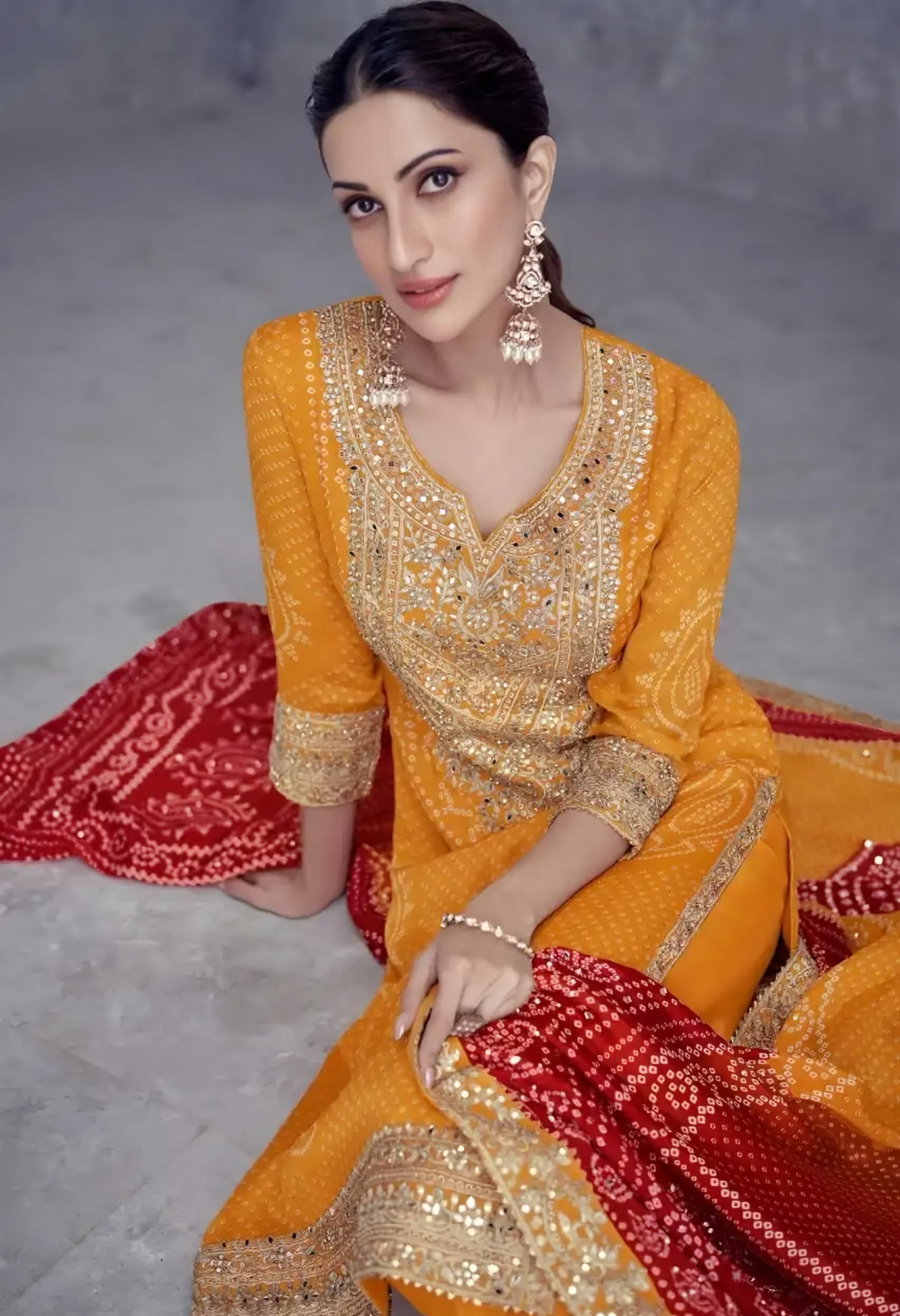 Woman in a traditional orange and red outfit with gold details sitting on a textured surface.