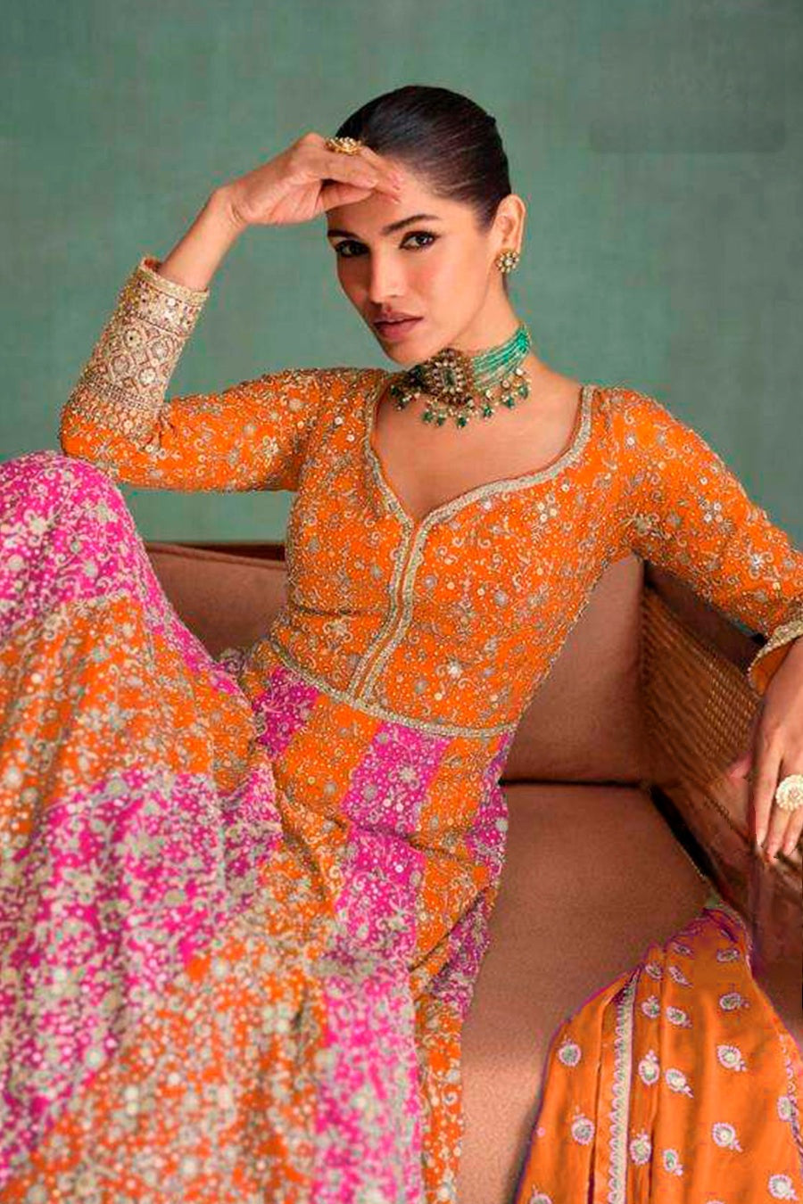 Woman in a colorful traditional outfit with an orange and pink dress against a green background