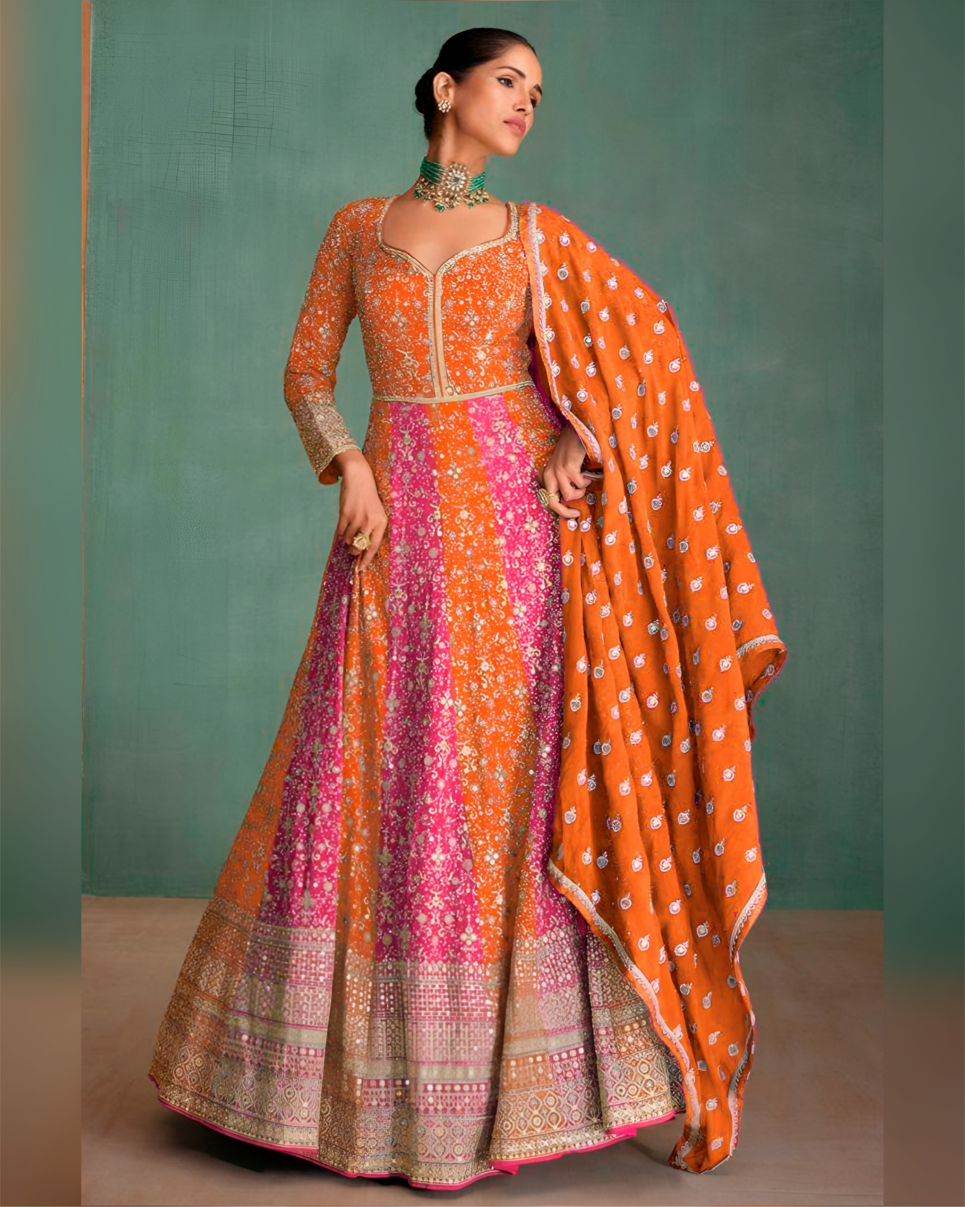 Woman wearing a traditional orange and pink outfit with a matching dupatta against a teal background