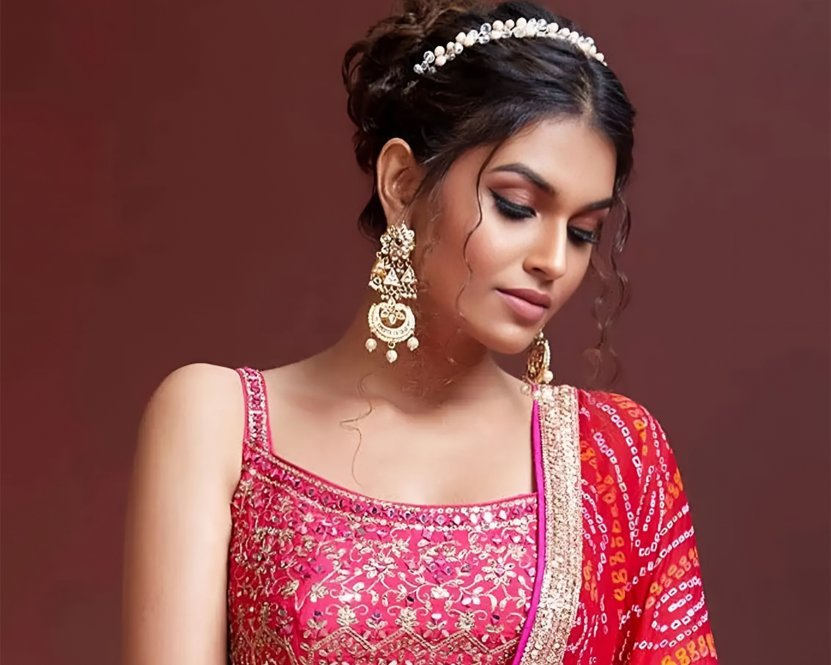 Woman wearing a traditional pink and red embroidered outfit with jewelry against a brown background