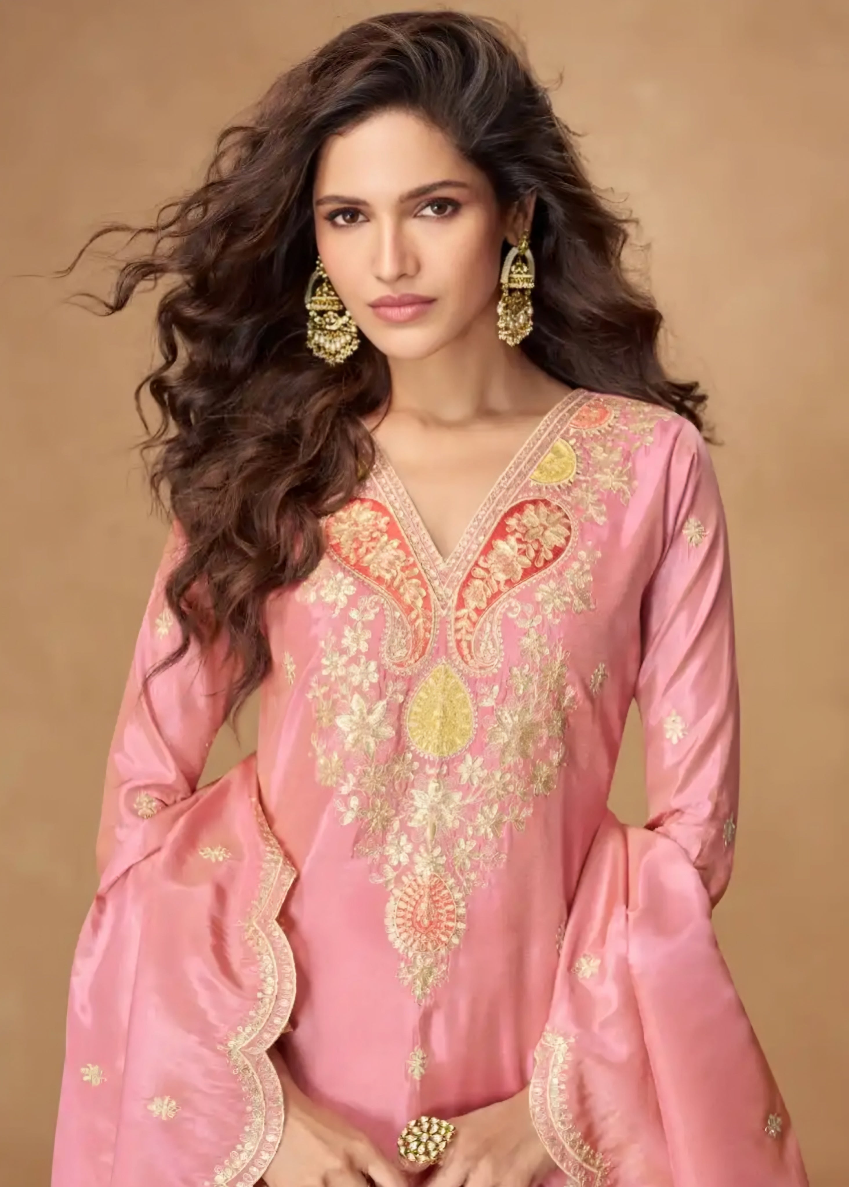 Woman wearing a pink embroidered traditional outfit with gold details on a beige background