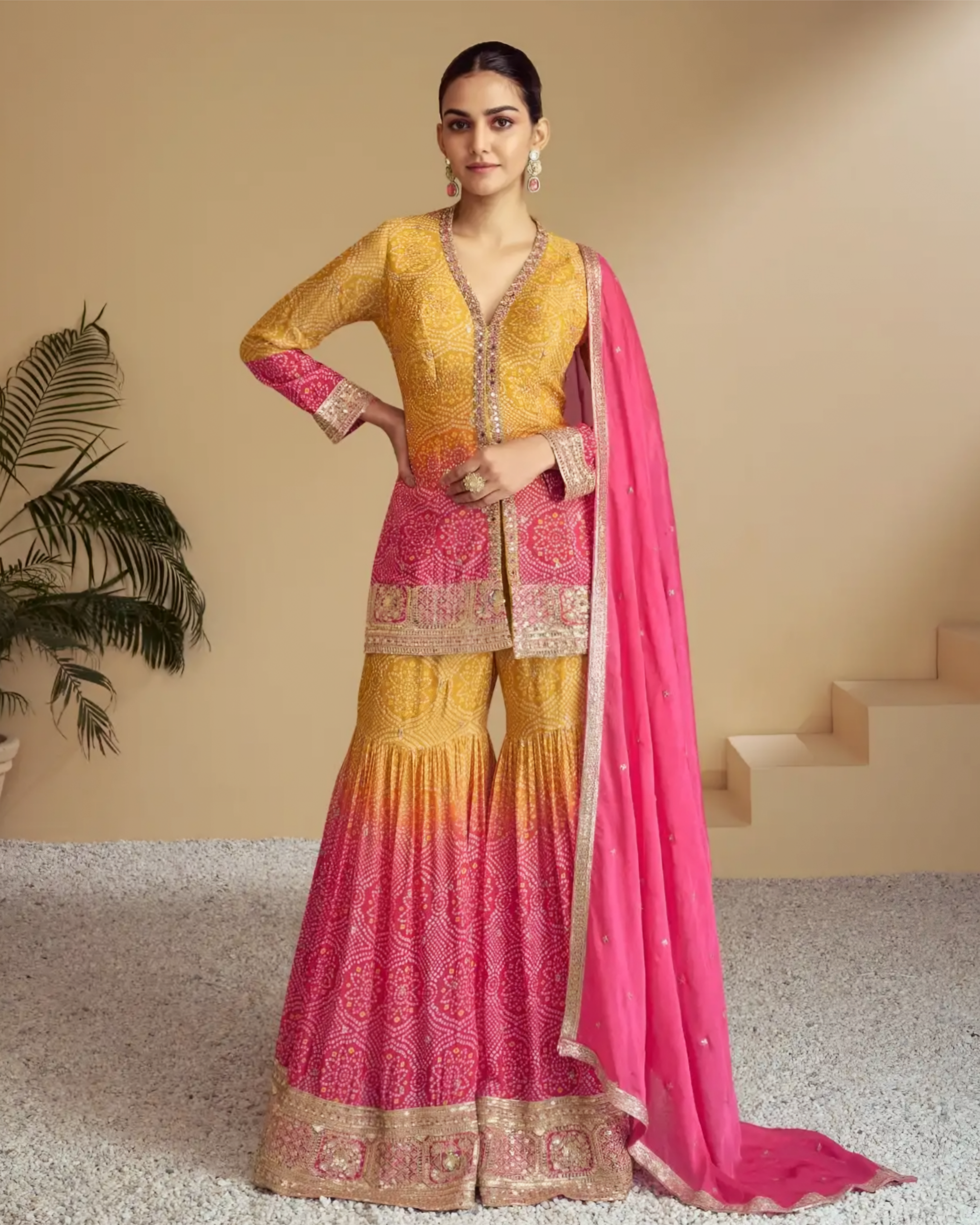Woman wearing a traditional outfit with a yellow and pink dress and dupatta in an indoor setting.